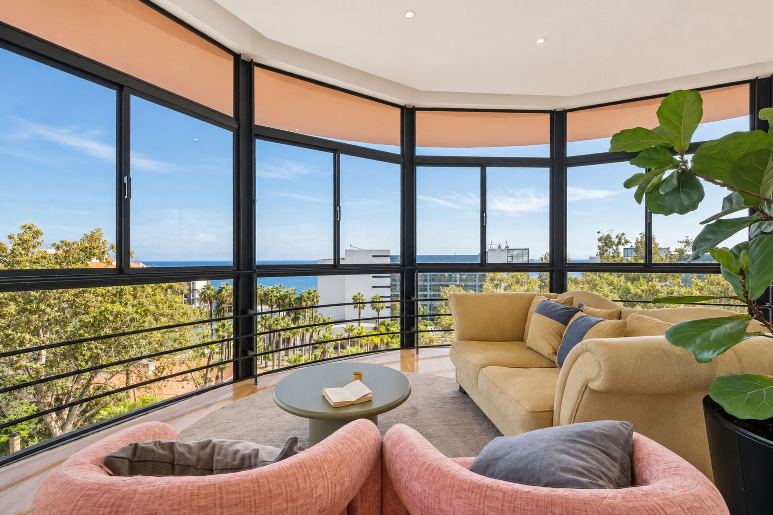 Een ruim balkon met uitzicht op zee en palmbomen, voorzien van een bank en een klein tafeltje.