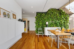 Eine moderne Küche mit einem Holztisch, weißen Stühlen und einer grünen Wand mit Blättern.
