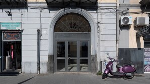 Rakennuksen sisäänkäynti, jossa on lasiovi ja sen ulkopuolella parkkeerattu skootteri.