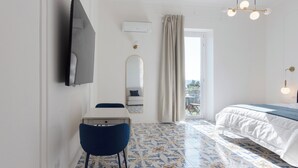 Hotellihuone, jossa on sänky, työpöytä tuolilla, seinälle asennettu televisio, peili ja ikkuna, jossa on verhot.
