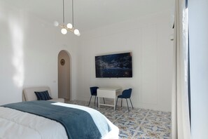 A bedroom with a bed, a desk, two chairs, a TV, and a patterned floor. - Sea view apartment Chiaia 150 near metro line 6 (Napoli)