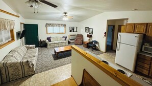 A living room with a sofa, armchair, and coffee table. There is a ceiling fan, a window with blinds, and a door.