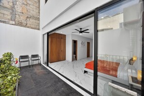A modern room with a large sliding glass door, a ceiling fan, and a bed with an orange blanket. - Unit Elote Romantic Zone (Puerto Vallarta)