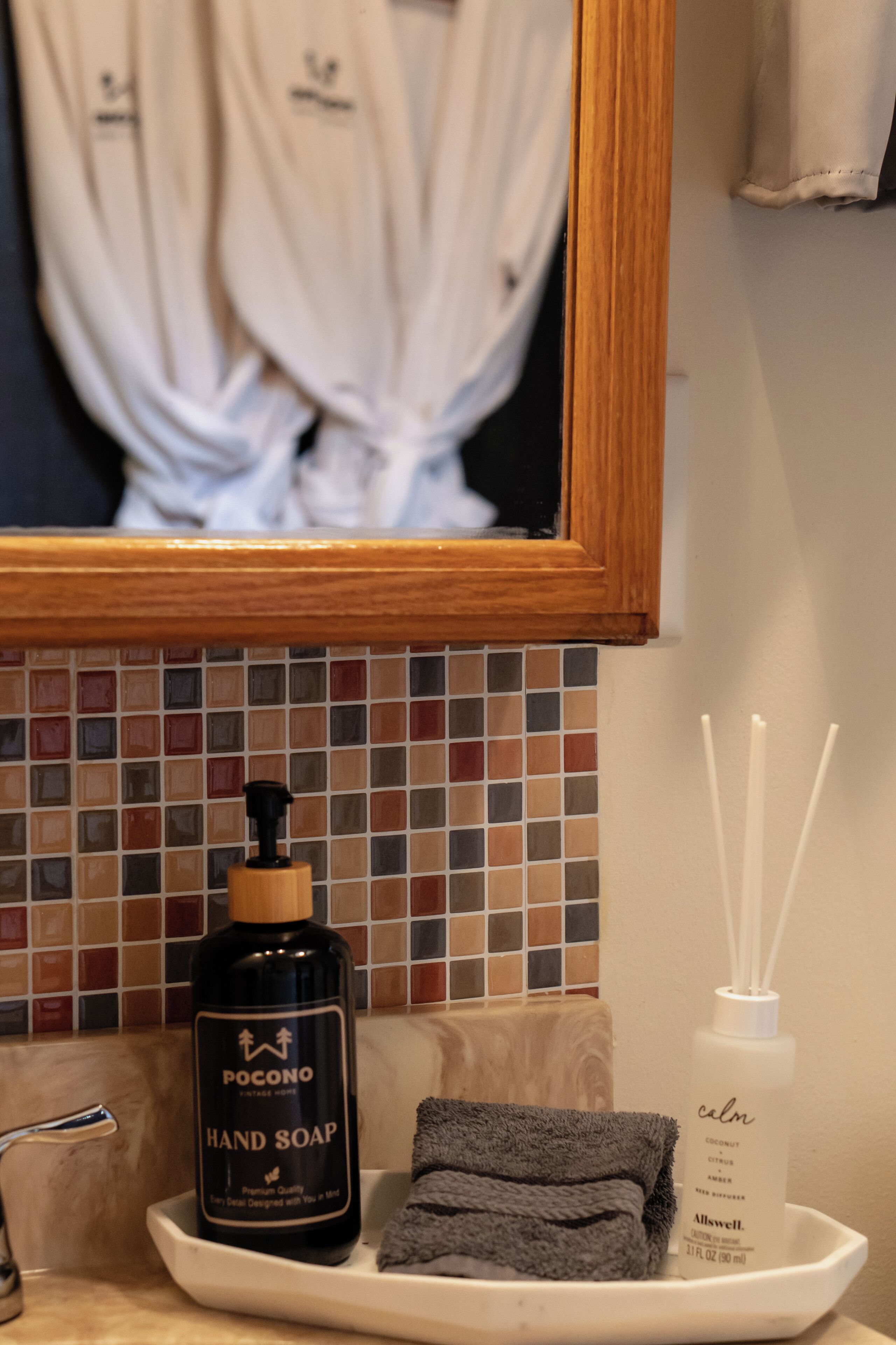 A bathroom counter with a bottle of Pocono hand soap, a towel, and a diffuser.
