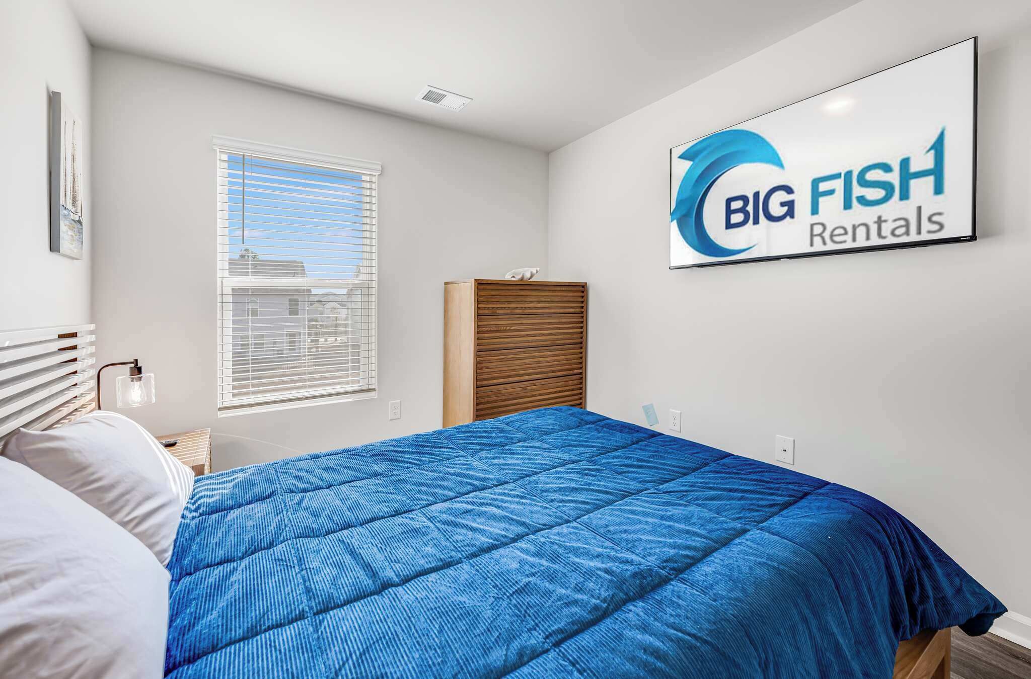 Un dormitorio con cama, una ventana con persianas, cabecero y un cartel en la pared de Big Fish Rentals.