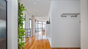 Ein moderner Flur mit Holzboden, einer weißen Wand mit einer schwarzen Vase und einer Pflanze auf der linken Seite.