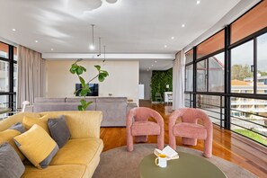 Uma sala de estar moderna com sofá, duas poltronas, mesa de centro e uma janela ampla com vista para prédios.