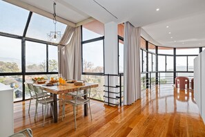 Un vaste espace dédié à la salle à manger, avec une table et des chaises en bois, de grandes fenêtres offrant une vue sur la ville et un design moderne au niveau du plafond.
