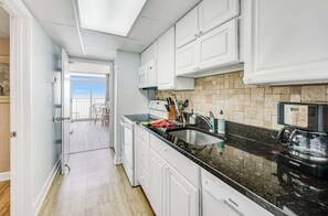A kitchen with white cabinets, a black countertop, and a coffee maker. - High Floor, Direct Oceanfront Views,Camelot Resort (Myrtle Beach)
