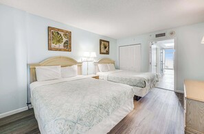 A hotel room with two beds, a wooden floor, a nightstand, and a door leading to a balcony. - High Floor, Direct Oceanfront Views,Camelot Resort (Myrtle Beach)