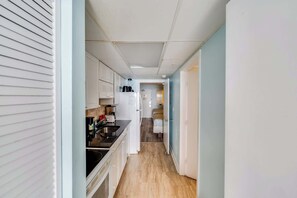 A narrow hallway leading to a kitchen with white cabinets, a black countertop, and a refrigerator. - High Floor, Direct Oceanfront Views,Camelot Resort (Myrtle Beach)
