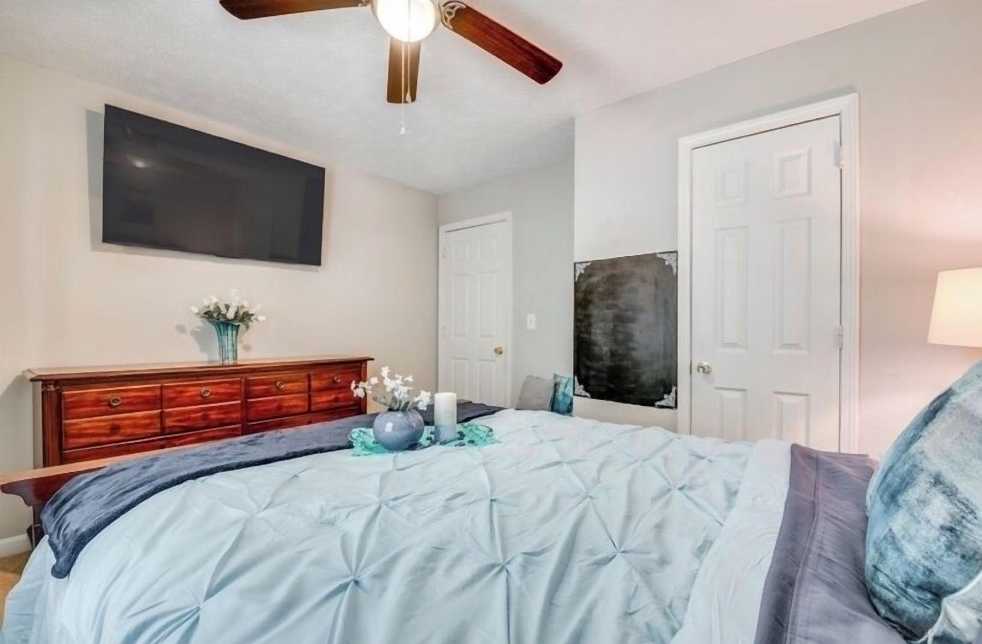 Ein Schlafzimmer mit einem Bett, einem Schminktisch, einem Deckenventilator und einem an der Wand befestigten Fernseher.