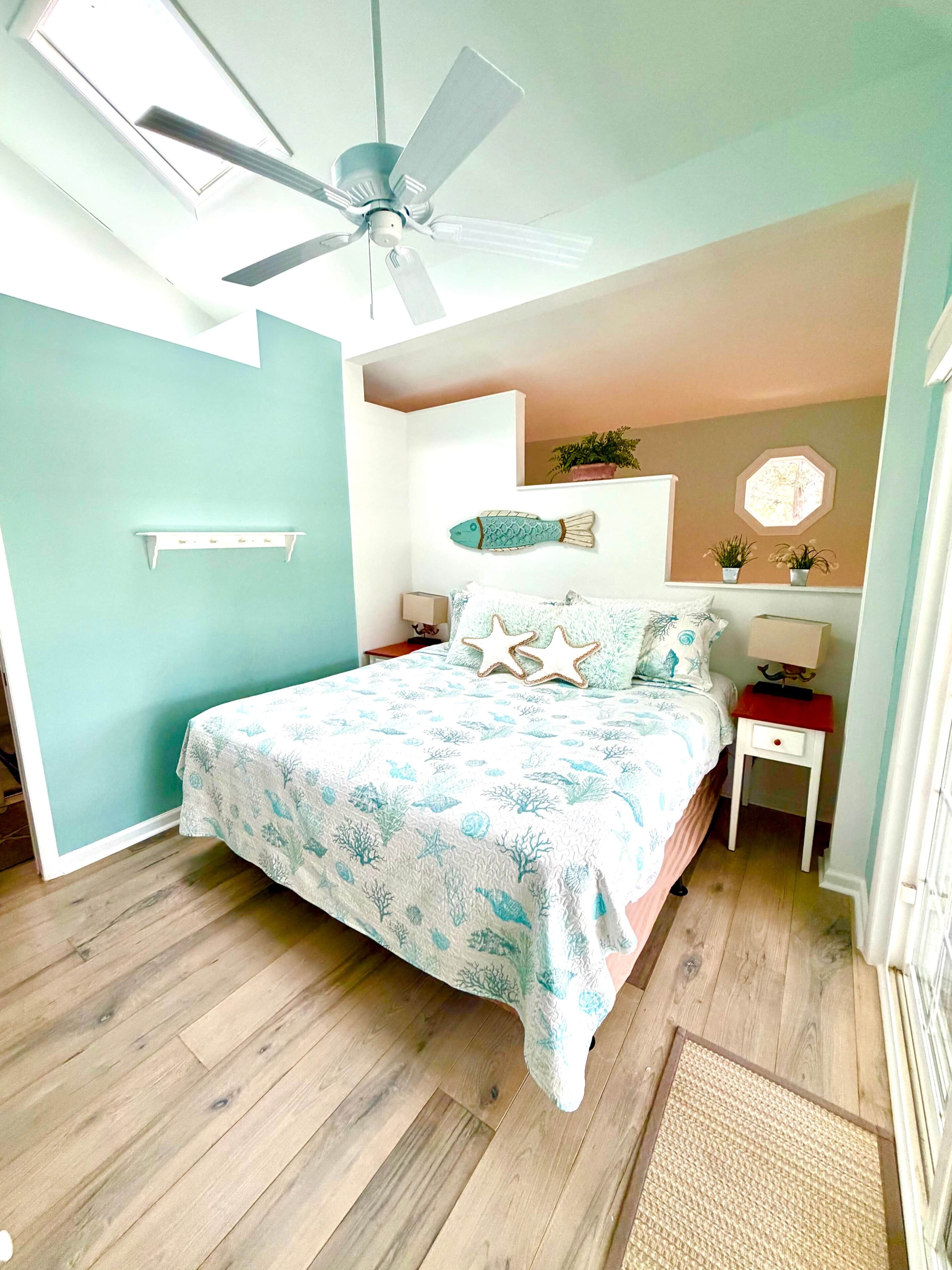 A bedroom with a bed, a ceiling fan, a nightstand, a wall-mounted shelf, and a window.