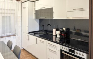 A modern kitchen with white cabinets, a black countertop, a sink, a coffee maker, and a stove. - Amazing apartment in Lukovo Sugarje with WiFi (Lukovo Sugarje)