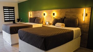 Hotellihuone, jossa on kaksi sänkyä, puinen pääty ja yöpöydällä olevat lamput sekä vihreä seinä.