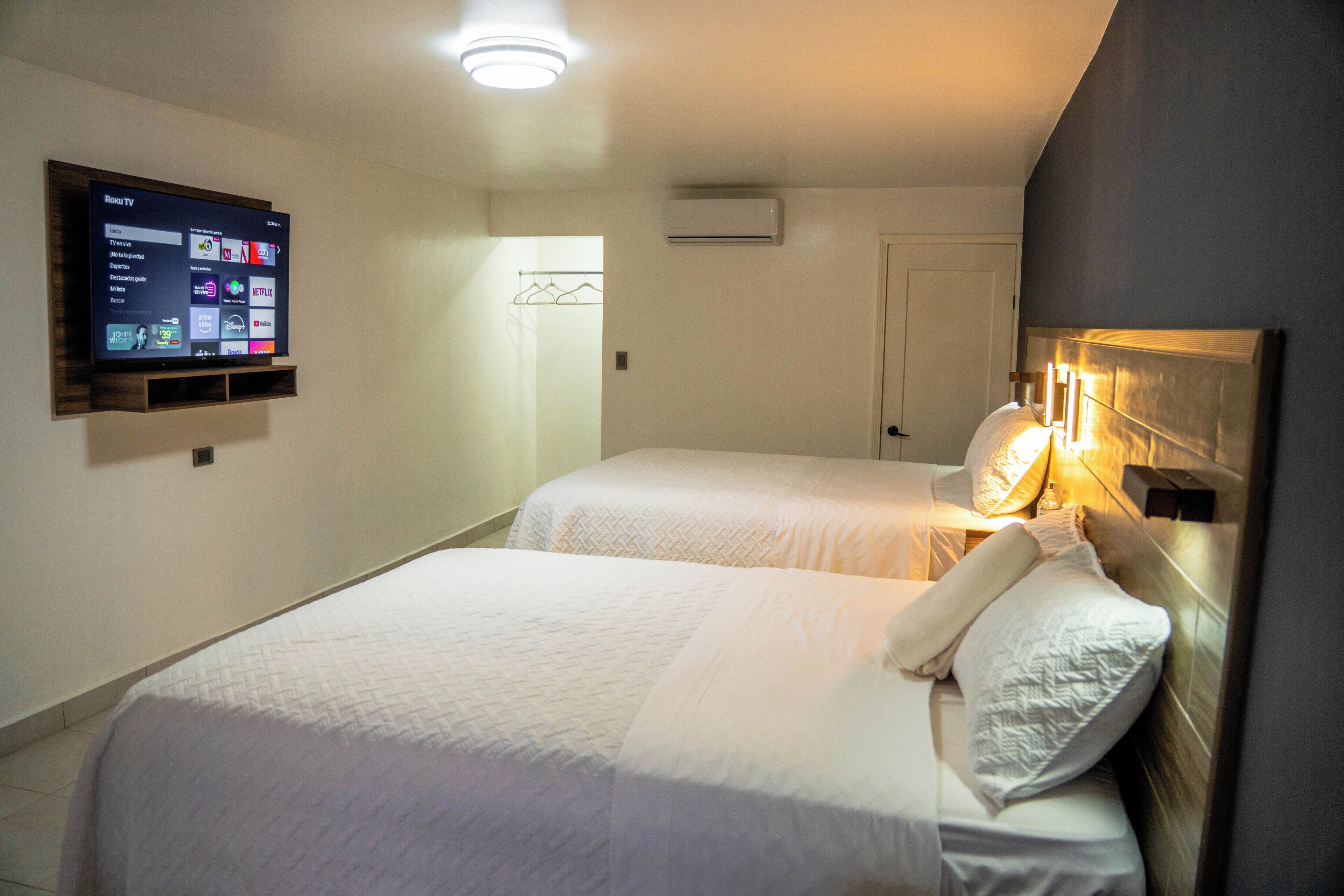 Habitació d'hotel amb dos llits, un televisor fixat a la paret i una porta que dóna a un passadís.