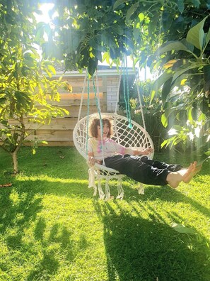 A person sitting in a hammock swing in a grassy outdoor area with trees and a wooden fence in the background. - Serene Family Holiday Home, Pillans Point - Tga (Tauranga)