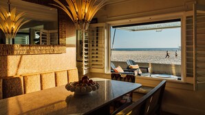 Habitación junto a la playa con un ventanal grande, una mesa de comedor y un frutero, y vistas a la playa.