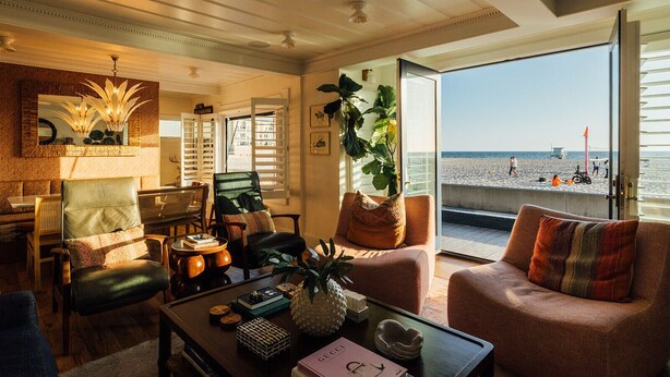 Una sala de estar con vista a la playa, un comedor con mobiliario de mimbre y una planta grande.