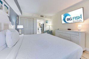 Une chambre d’hôtel avec un grand lit, une commode, un téléviseur diffusant des programmes de « Big Fish Rentals », et une vue sur la cuisine.