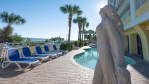 A poolside area with lounge chairs, a statue, and a building with balconies. - Honeymoon Suite with Direct Oceanfront View,Pools! (Myrtle Beach)