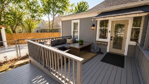 Une terrasse avec un canapé et une table, une clôture en bois et une maison dotée d’un porche.