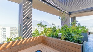 Eine moderne Dachterrasse mit Holzmöbeln, Blumentöpfen und Blick auf ferne Berge.