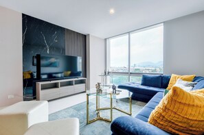 Una sala de estar moderna con un televisor grande, un sofá azul y un cojín amarillo.