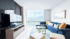 Ein modernes Wohnzimmer mit einem großen Fernseher, einem blauen Sofa und einem Glastisch.