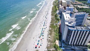 An aerial view of a beach with numerous umbrellas and people, adjacent to high-rise buildings. - Oceanview 1BR Condo • Kid-Friendly Resort • Pools + Arcade (Myrtle Beach)