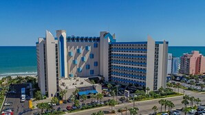 A hotel with a modern design, featuring a prominent tower and a parking lot with several cars. - Oceanview 1BR Condo • Kid-Friendly Resort • Pools + Arcade (Myrtle Beach)
