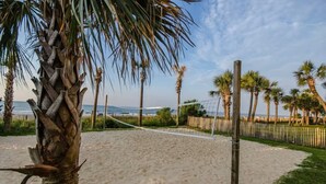 A sandy beach with a volleyball net, palm trees, and a wooden fence. - Oceanview 1BR Condo • Kid-Friendly Resort • Pools + Arcade (Myrtle Beach)