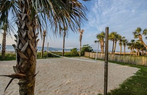 A sandy beach with a volleyball net, palm trees, and a wooden fence. - Oceanview 1BR Condo • Kid-Friendly Resort • Pools + Arcade (Myrtle Beach)