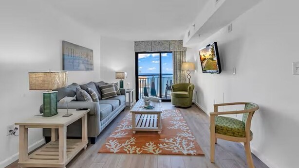 A modern living room with a grey sofa, a wooden coffee table, and a green armchair. - Oceanview 1BR Condo • Kid-Friendly Resort • Pools + Arcade (Myrtle Beach)