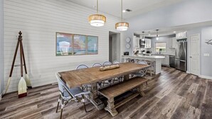 A modern kitchen with a wooden dining table, pendant lights, and a large island.