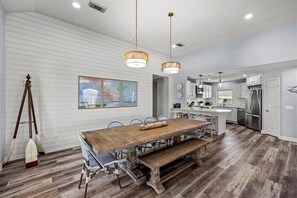 A modern kitchen with a wooden dining table, pendant lights, and a large island.