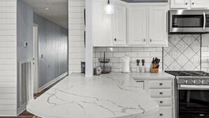 A kitchen with white cabinets, a marble countertop, a stainless steel microwave, and a gas stove.