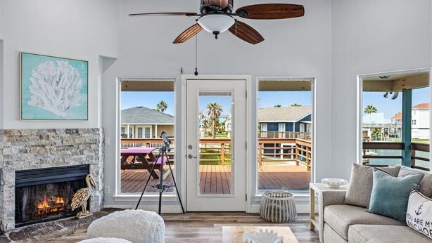A living room with a fireplace, a ceiling fan, and a view of a deck and pool.