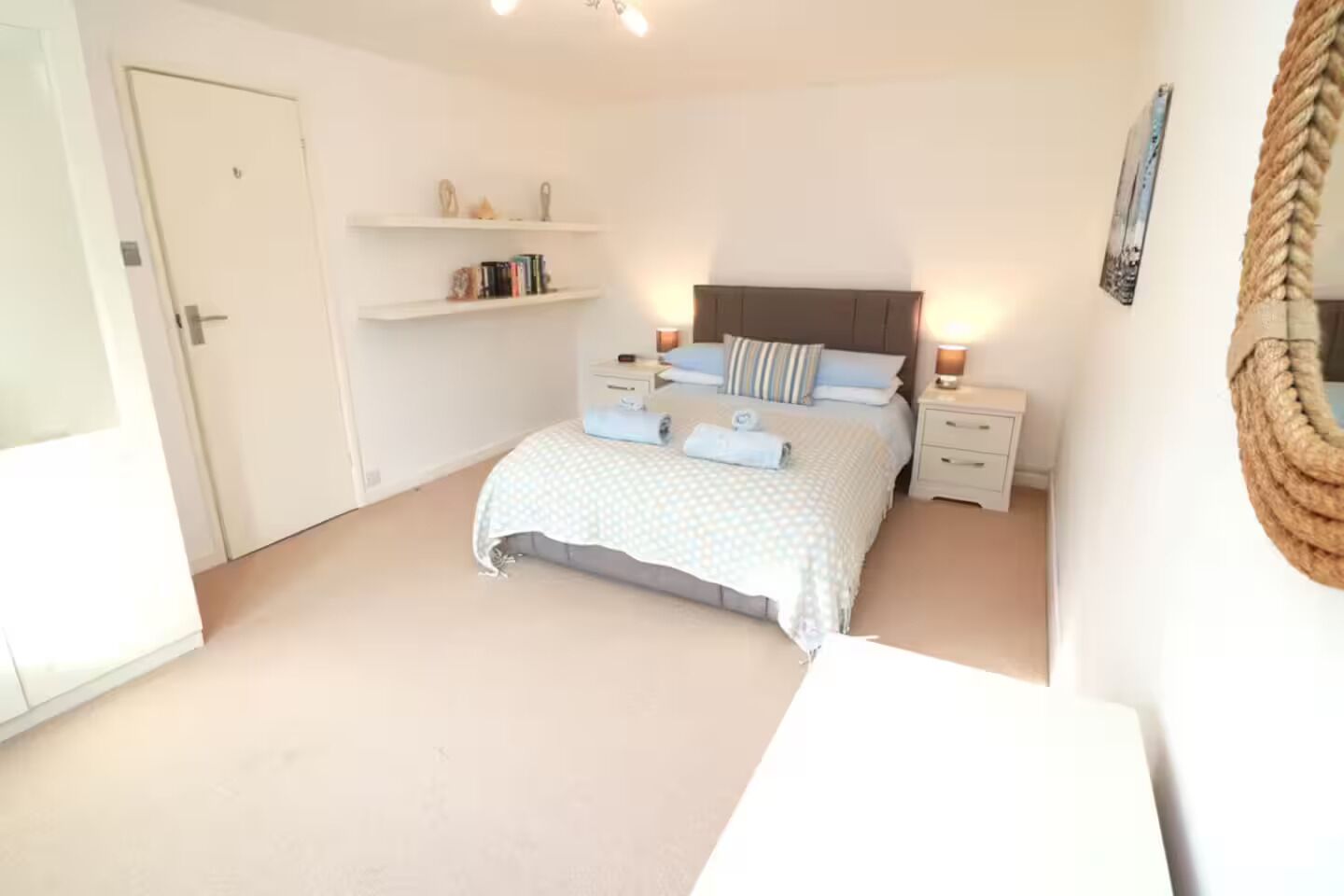 A bedroom with a bed, bedside tables, a wardrobe, and shelves with books and decorative items.