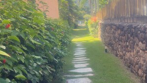 A pathway with stepping stones leading through a garden area with lush greenery and a stone wall on one side. - Experience Maresias to the fullest: with your feet in the sand, comfort, and exclusivity. (São Sebastião)