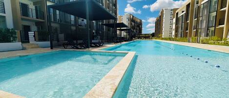A swimming pool with lounge chairs and umbrellas, surrounded by modern buildings with balconies.
