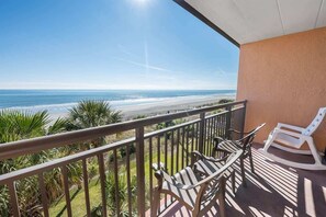 A balcony with a view of the beach, two striped lounge chairs, and a white rocking chair. - Caravelle withPools- Newly Added - Direct Oceanfront (Myrtle Beach)