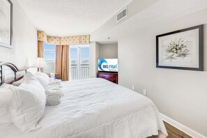 Une chambre d’hôtel avec un lit bien fait, une télévision, un tableau encadré et une vue sur l’extérieur.