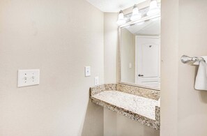 A bathroom with a granite countertop, a mirror, a towel rack, and a door. - 2BR Direct Oceanfront at Carolinian, Pools, Views! (Myrtle Beach)
