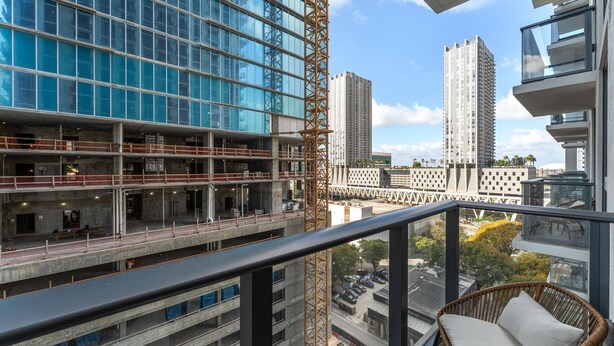 Un balcó amb una cadira de vimetes, davant d'una zona de construcció amb edificis moderns i una grua.