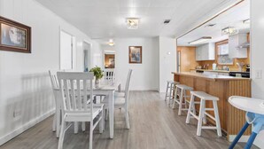 Een moderne keuken met witte kastjes, een houten aanrechtblad en een eethoek met witte stoelen en een tafel.