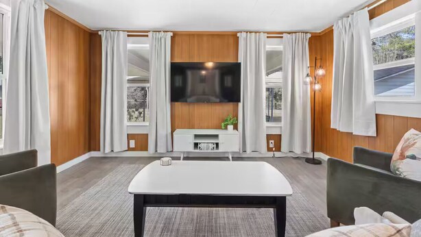Een moderne woonkamer met een flatscreen televisie aan de muur, een witte salontafel en twee stoelen.