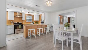 Een moderne keuken met houten kastjes, een centraal kookeiland met krukken, en een eethoek met witte stoelen.