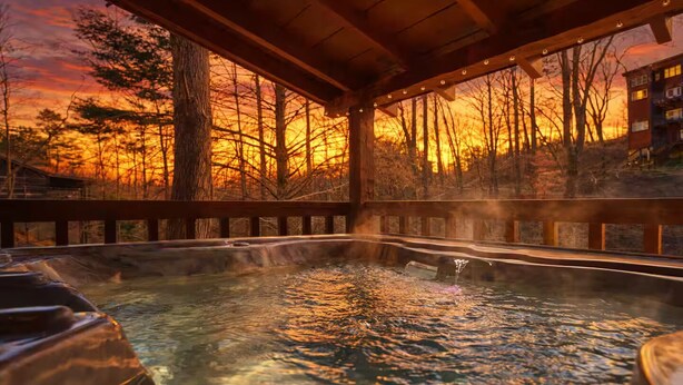 A hot spring area with a wooden deck and a view of trees and a sunset. - Peace, Quiet, and a Cozy Cabin (Sevierville)