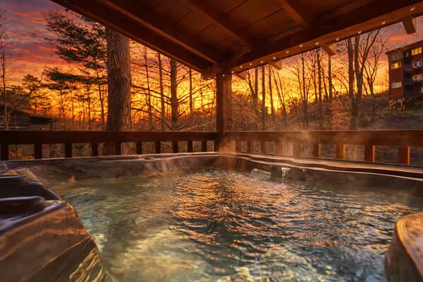 A hot spring area with a wooden deck and a view of trees and a sunset. - Peace, Quiet, and a Cozy Cabin (Sevierville)